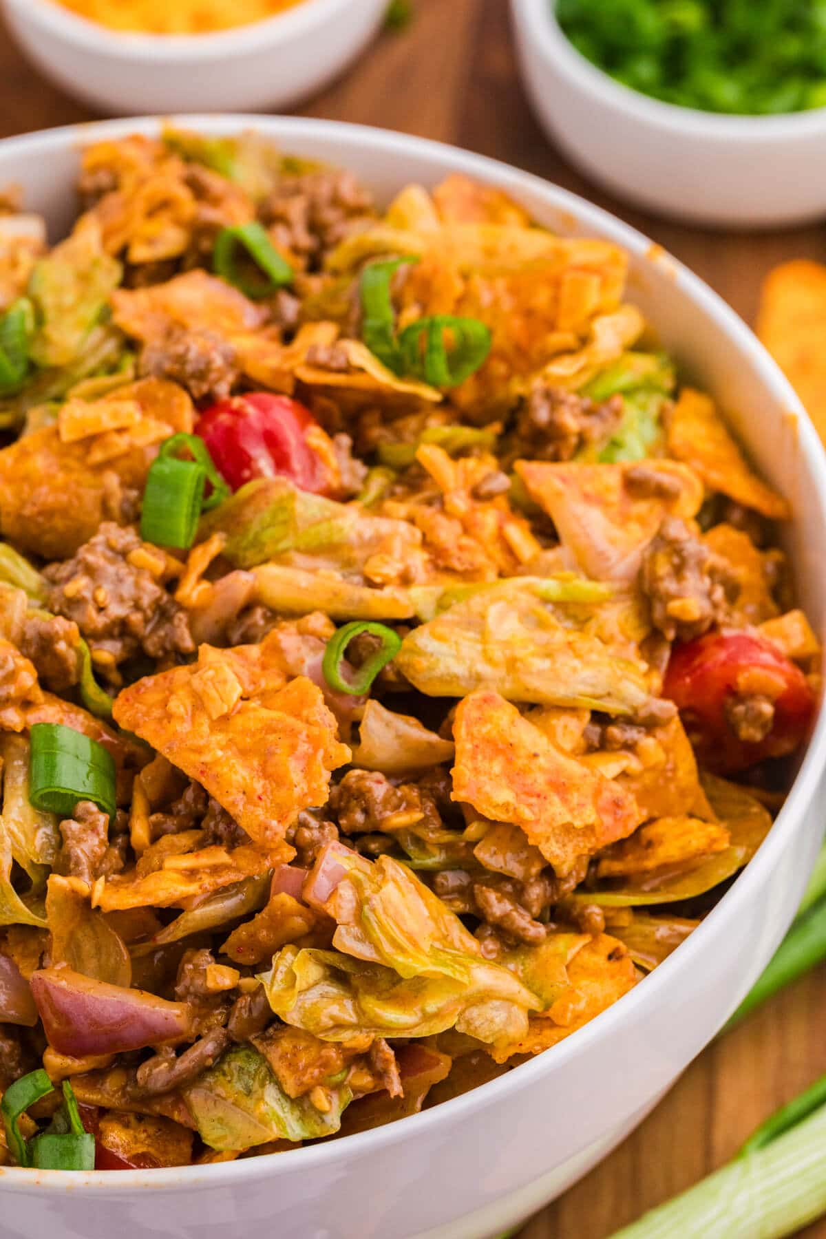 Close-up of Dorito Taco Salad with seasoned ground beef, iceberg lettuce, cherry tomatoes, red onion, cheddar cheese, green onions, and crushed nacho cheese Doritos.