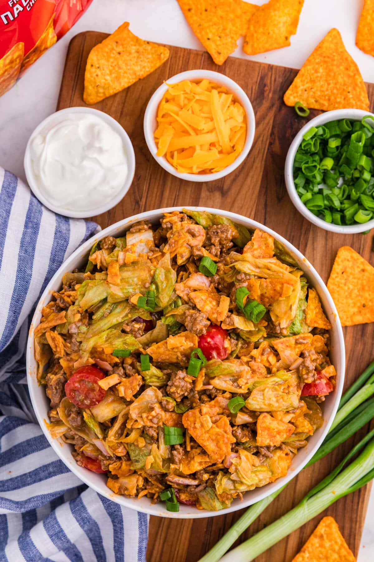 Dorito Taco Salad in a white bowl with seasoned ground beef, iceberg lettuce, cherry tomatoes, cheddar cheese, green onions, and crushed nacho cheese Doritos.