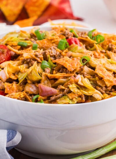 Bowl of Dorito Taco Salad with seasoned ground beef, lettuce, tomatoes, red onion, cheddar cheese, green onions, and crushed nacho cheese Doritos.