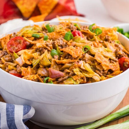 Bowl of Dorito Taco Salad with seasoned ground beef, lettuce, tomatoes, red onion, cheddar cheese, green onions, and crushed nacho cheese Doritos.