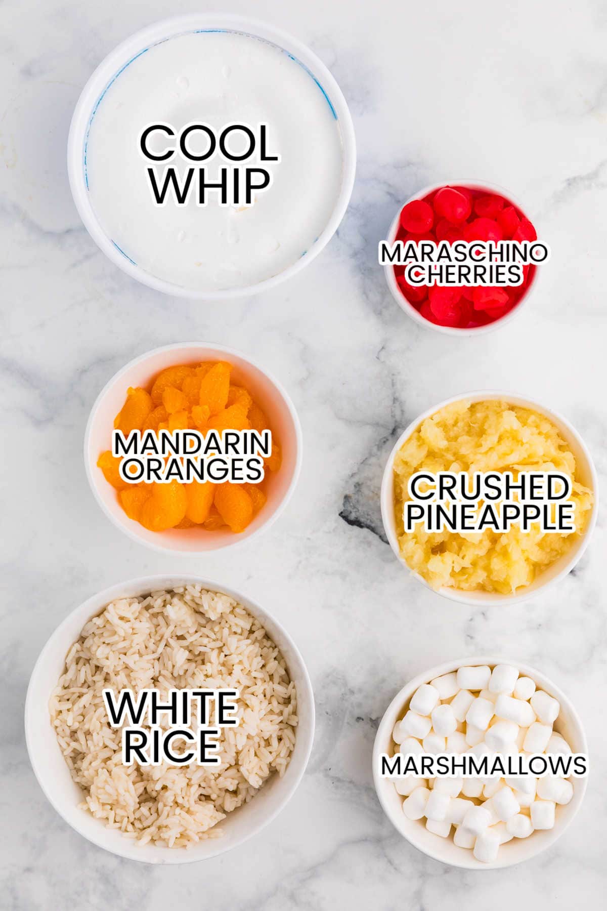 Six bowls arranged on a white marble surface show the ingredients for glorified rice.