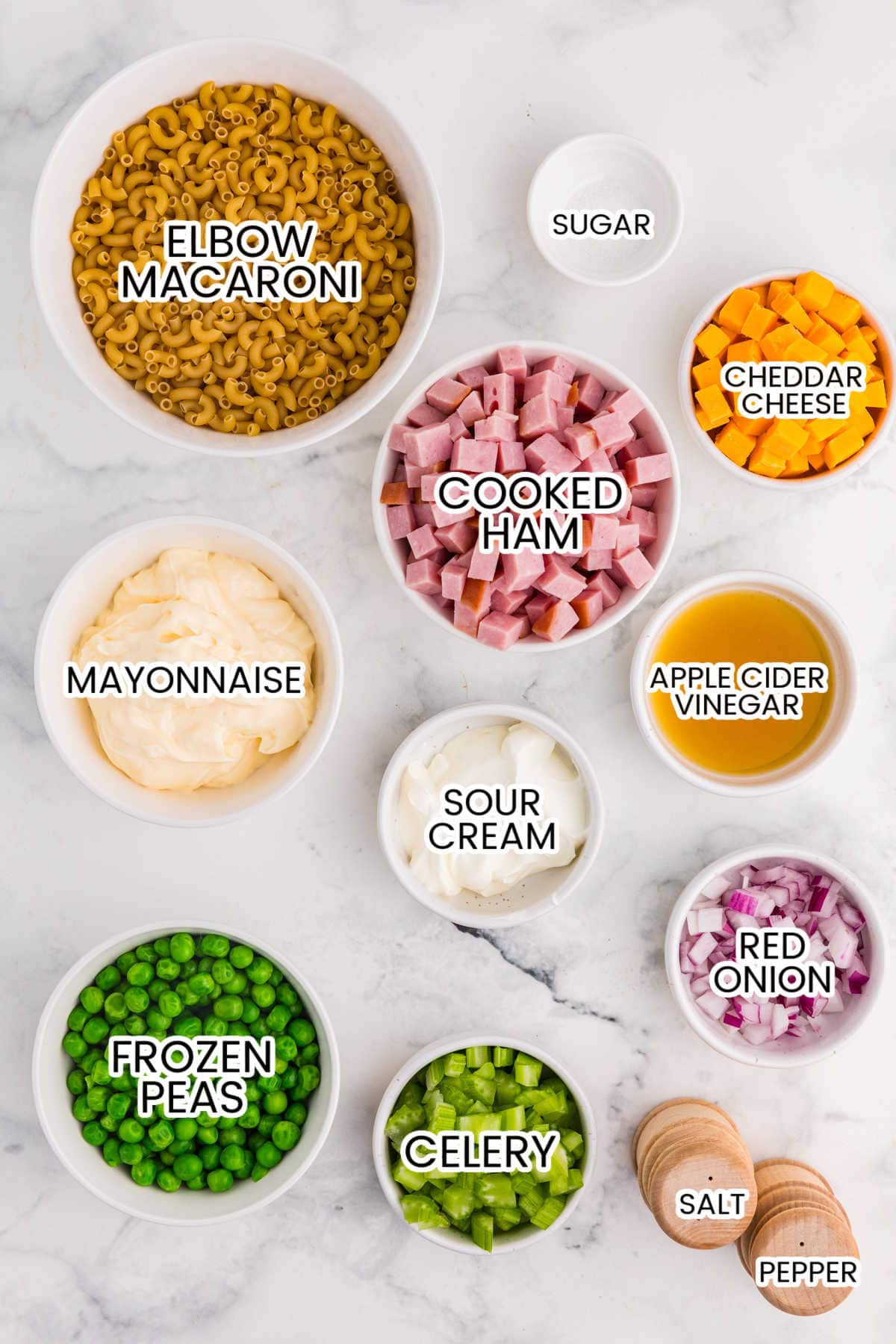 Overhead layout of ingredients for ham and pea pasta salad on a marble countertop.