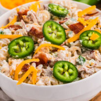 Bowl of creamy Jalapeño Popper Pasta Salad topped with fresh jalapeño slices, shredded cheddar cheese, and crispy bacon.