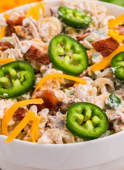 Bowl of creamy Jalapeño Popper Pasta Salad topped with fresh jalapeño slices, shredded cheddar cheese, and crispy bacon.