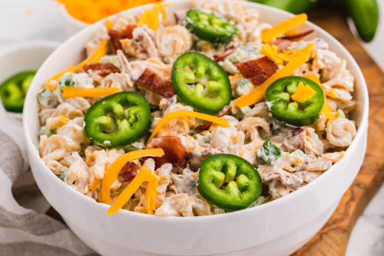 Bowl of creamy Jalapeño Popper Pasta Salad topped with fresh jalapeño slices, shredded cheddar cheese, and crispy bacon.