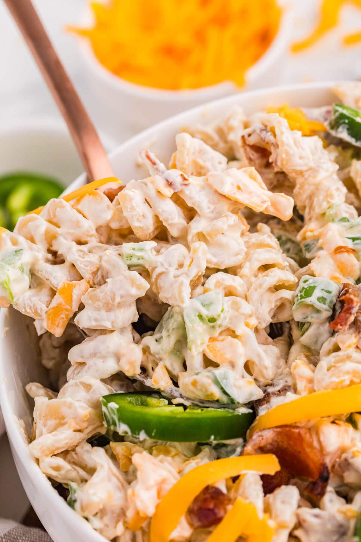 Serving spoon lifting creamy Jalapeño Popper Pasta Salad with rotini, cheddar cheese, bacon, green onions, and sliced jalapeños.