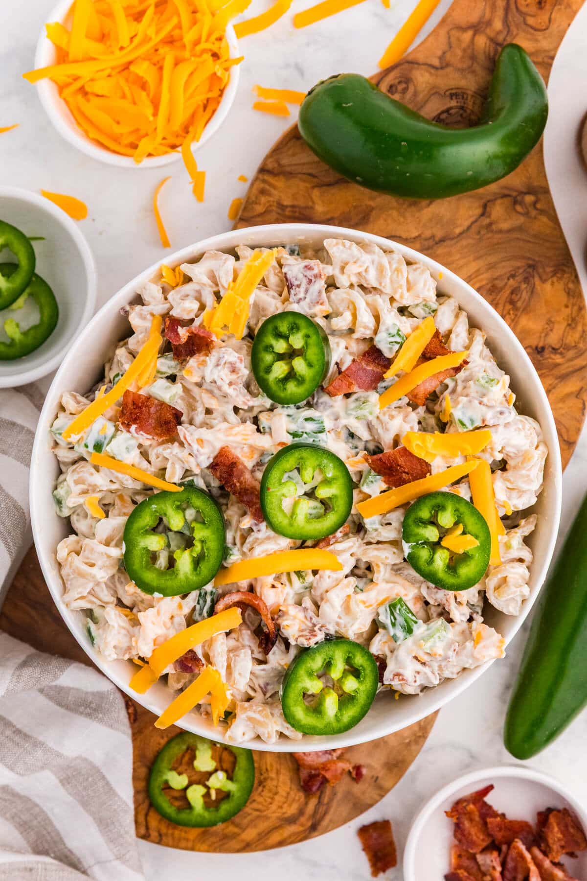 Overhead view of creamy Jalapeño Popper Pasta Salad topped with sliced jalapeños, shredded cheddar cheese, and crispy bacon.