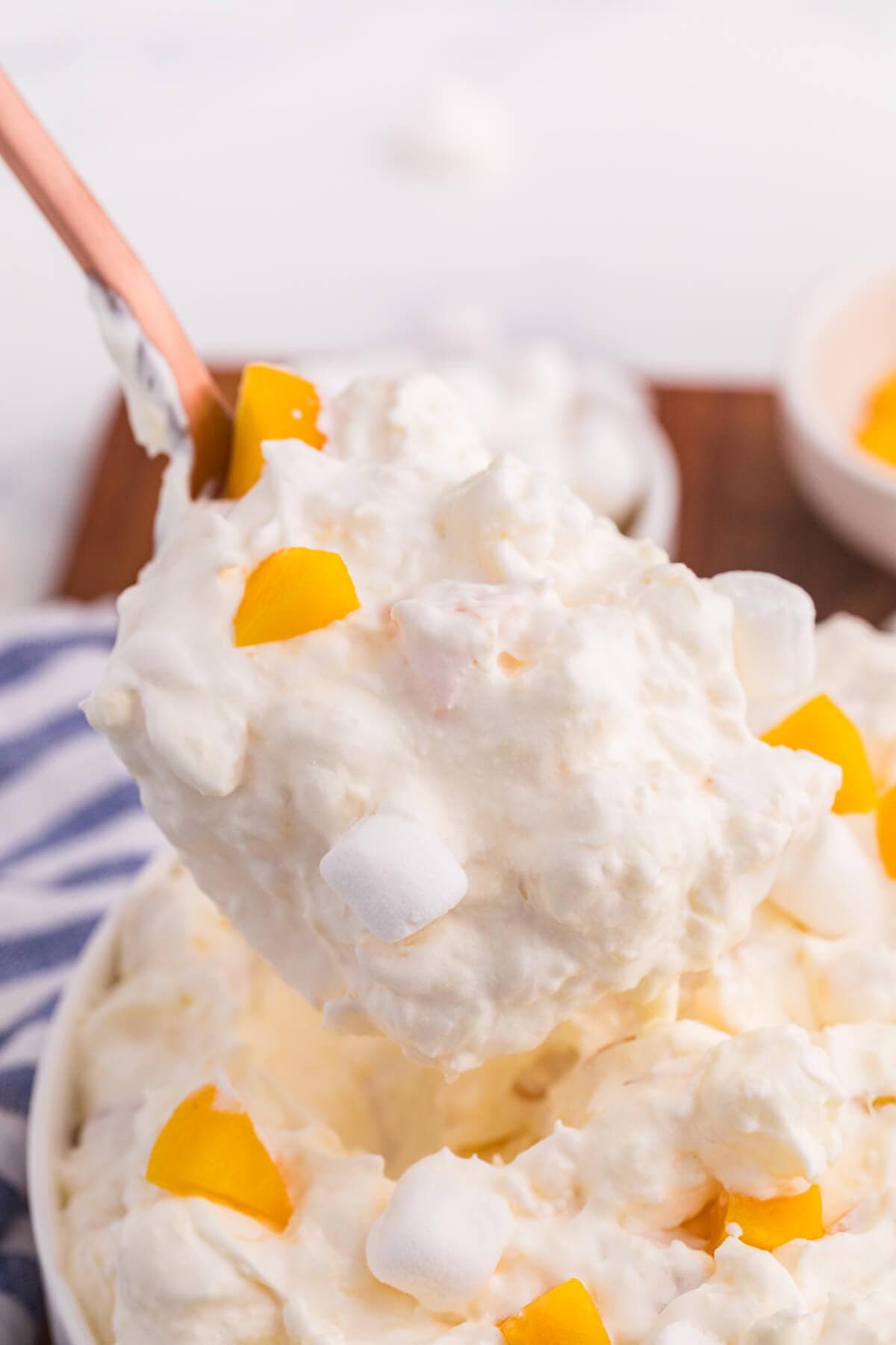 Spoonful of creamy peach fluff salad with chopped peaches and mini marshmallows being lifted from a serving bowl.
