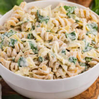 Creamy spinach artichoke pasta salad with rotini, spinach, artichokes, and cheese in a white serving bowl.