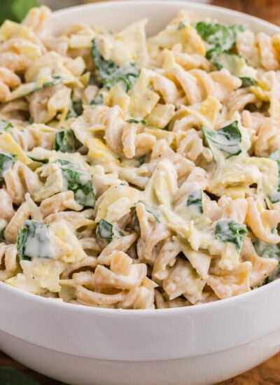 Creamy spinach artichoke pasta salad with rotini, spinach, artichokes, and cheese in a white serving bowl.
