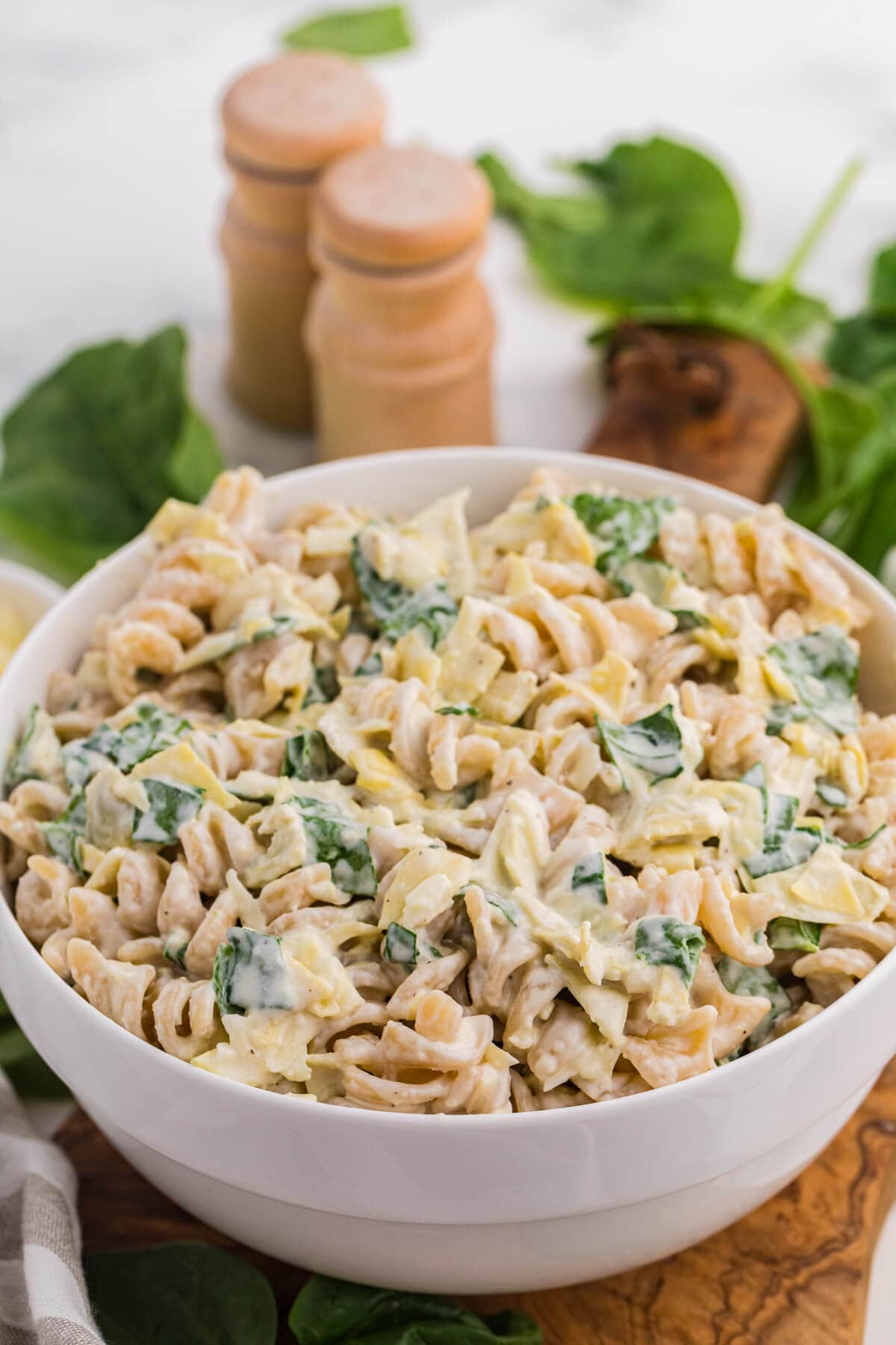 Creamy spinach artichoke pasta salad with rotini, chopped spinach, artichokes, and cheese in a white serving bowl.