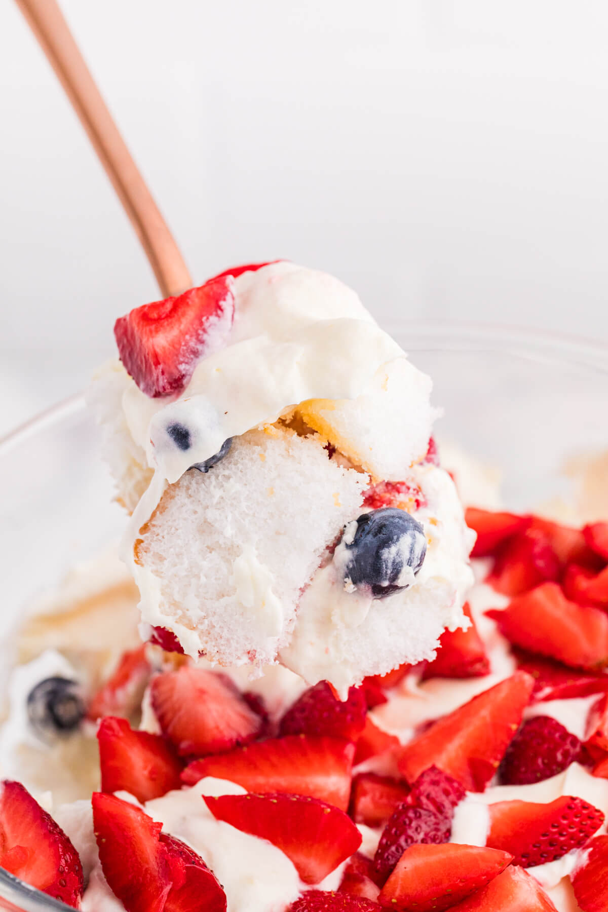 Close-up of a spoonful of Angel Food Cake Trifle with fluffy cake, creamy vanilla filling, strawberries, and blueberries.