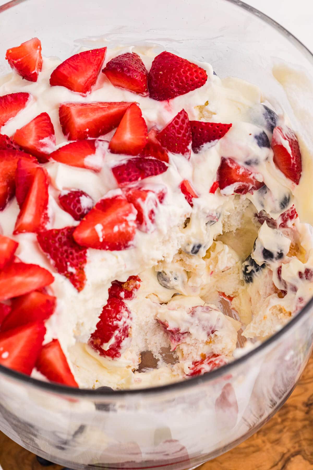 Partially served Angel Food Cake Trifle showing layers of fluffy cake, creamy vanilla filling, strawberries, blueberries, and raspberries.