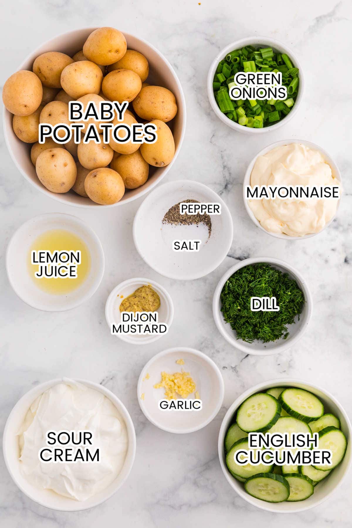 Overhead view of cucumber potato salad ingredients, including baby potatoes, English cucumber, sour cream, mayonnaise, dill, and green onions.