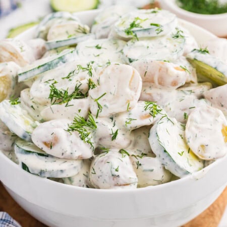 Creamy cucumber potato salad with baby potatoes, sliced cucumber, and fresh dill in a white serving bowl.
