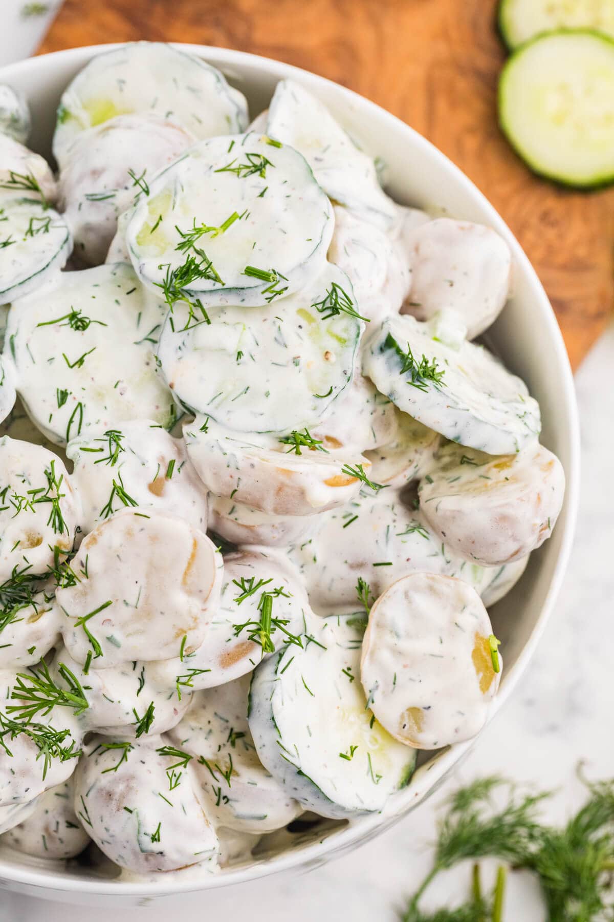 Close-up of creamy cucumber potato salad with baby potatoes, cucumber slices, and fresh dill in a white bowl.