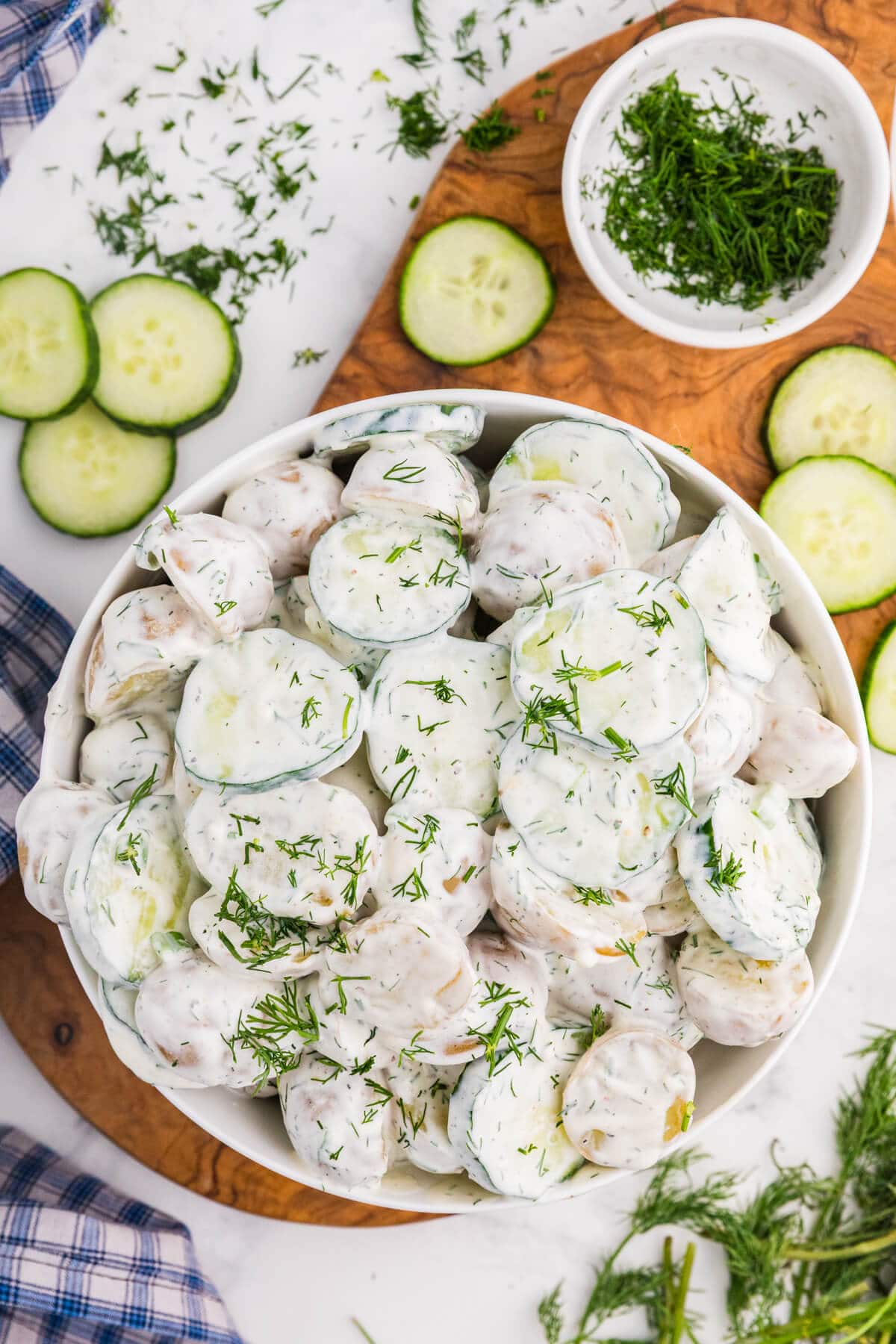 Overhead view of creamy cucumber potato salad with baby potatoes, sliced cucumber, and fresh dill in a white bowl.