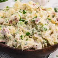 Creamy roasted garlic potato salad with red potatoes, celery, green onions, and parsley served in a wooden bowl.
