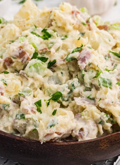 Creamy roasted garlic potato salad with red potatoes, celery, green onions, and parsley served in a wooden bowl.