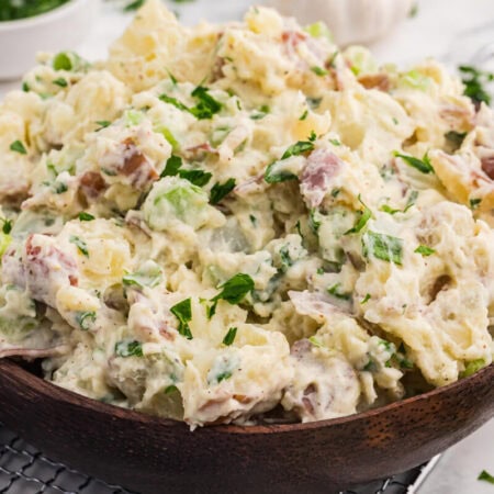 Creamy roasted garlic potato salad with red potatoes, celery, green onions, and parsley served in a wooden bowl.