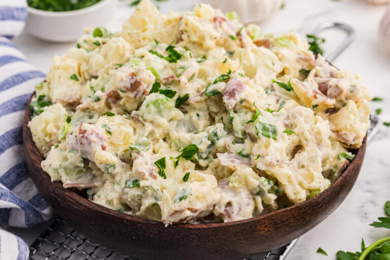 Creamy roasted garlic potato salad with red potatoes, celery, green onions, and parsley served in a wooden bowl.
