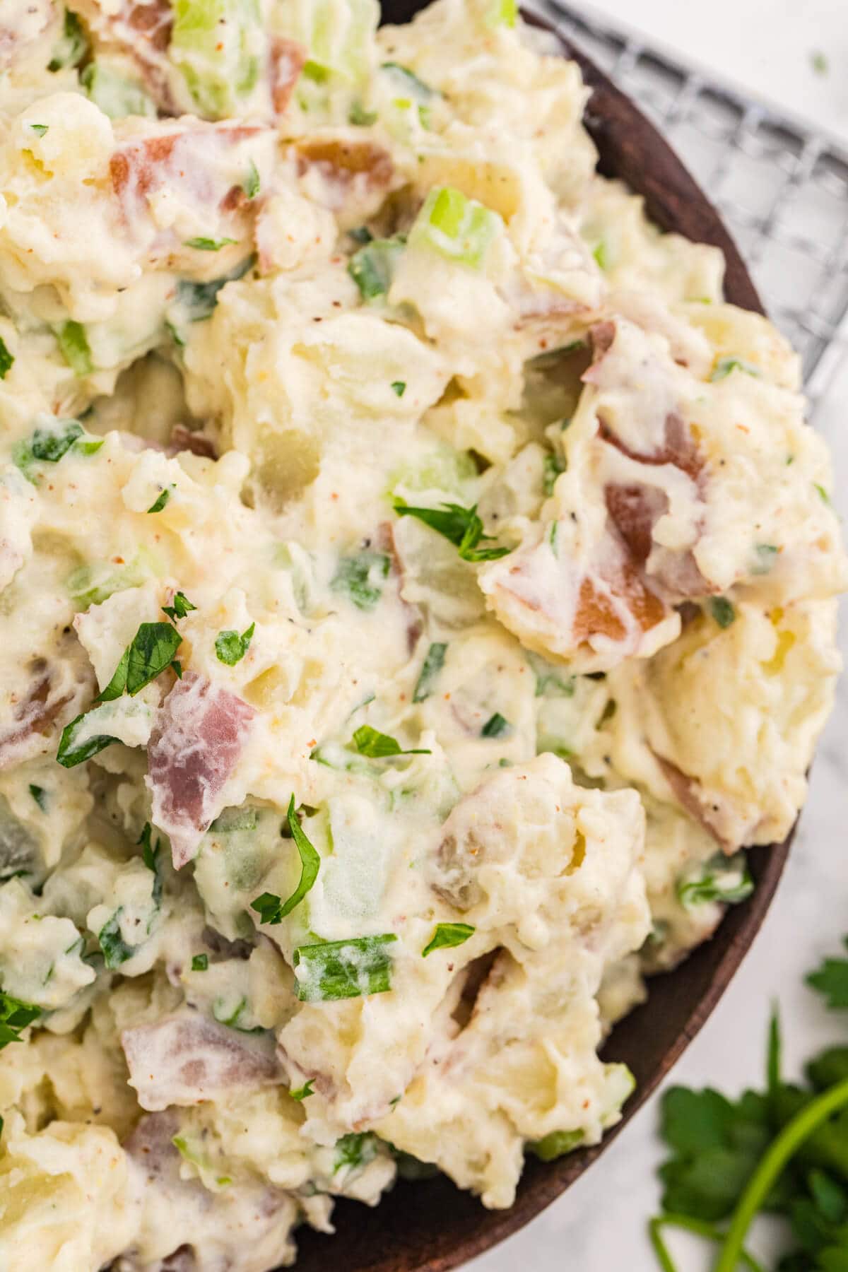 Close-up of creamy roasted garlic potato salad with red potatoes, celery, green onions, and chopped parsley.