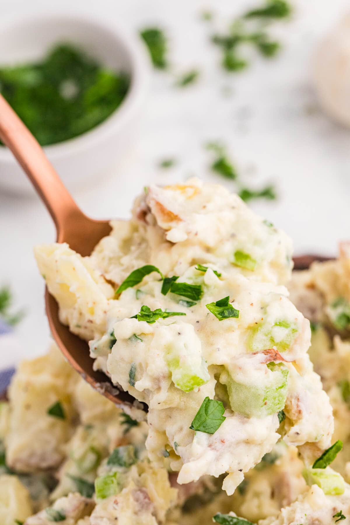 Spoonful of creamy roasted garlic potato salad with red potatoes, celery, green onions, and fresh parsley.