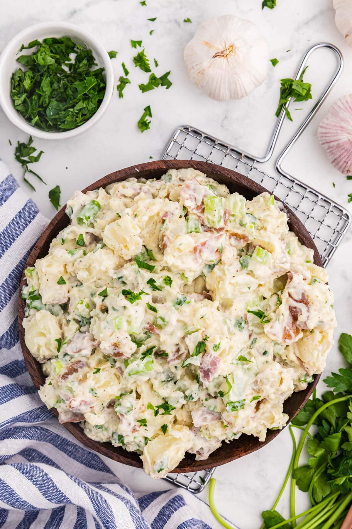 Overhead view of creamy roasted garlic potato salad with red potatoes, celery, green onions, and parsley in a wooden bowl.