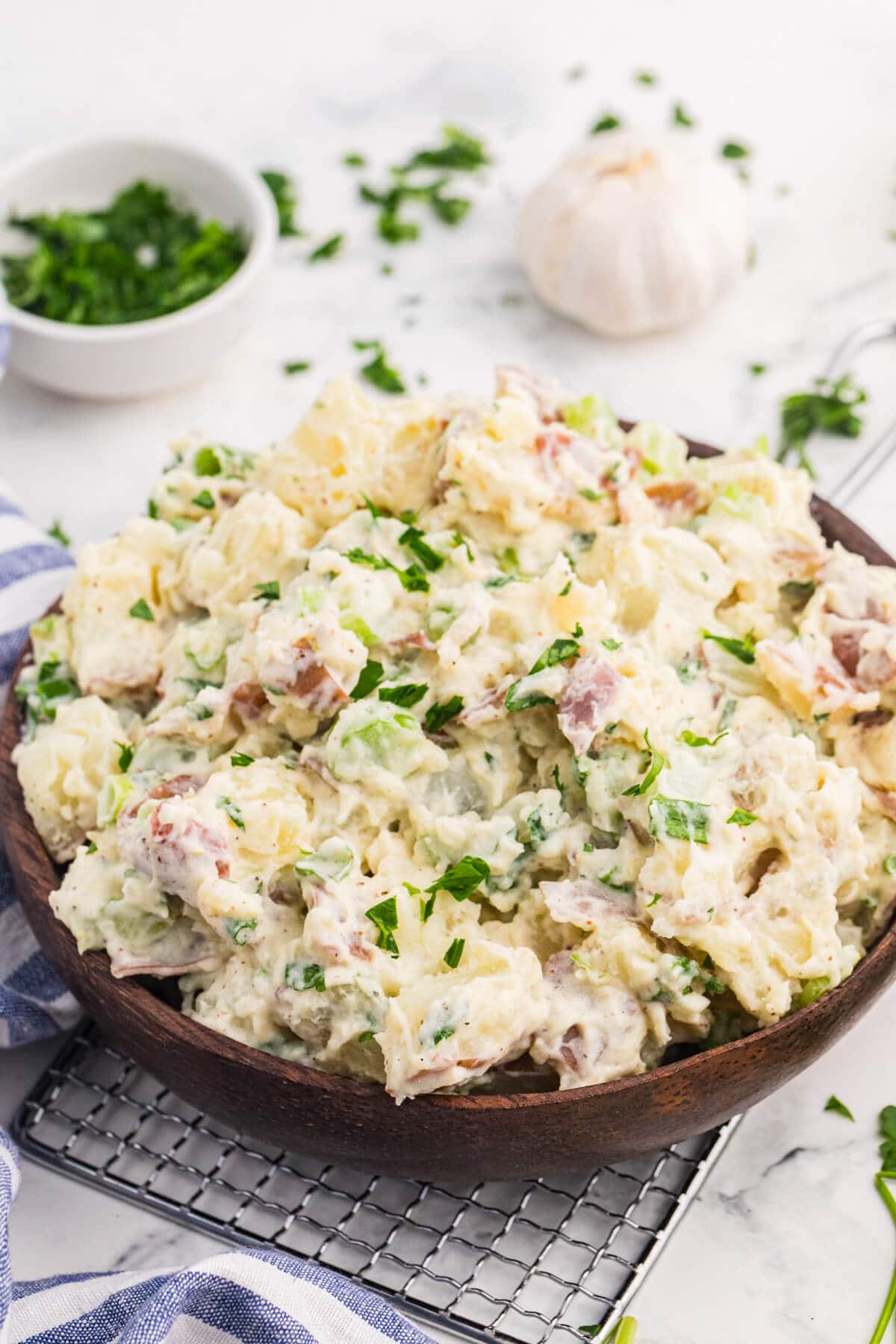 Close-up of creamy roasted garlic potato salad with red potatoes, celery, green onions, and fresh parsley in a wooden bowl.