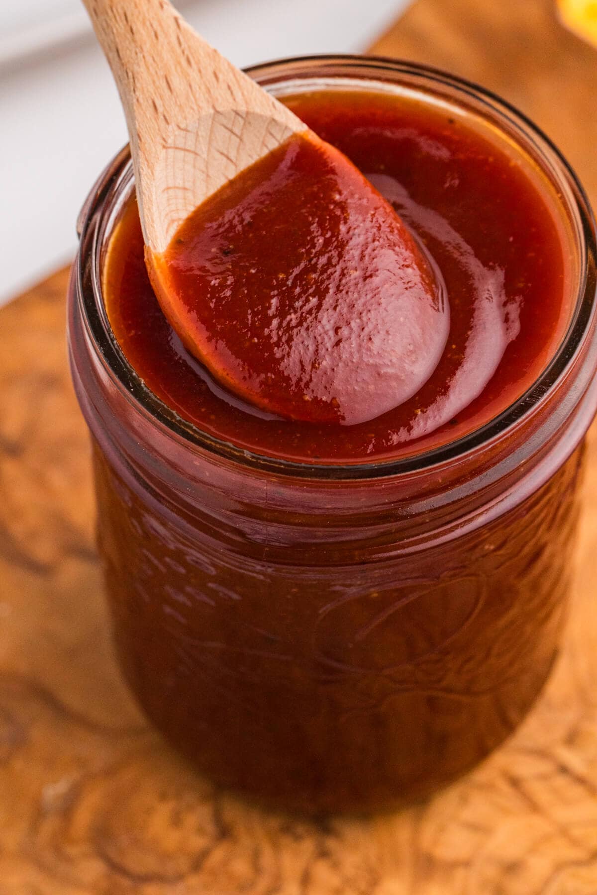 Close-up of thick homemade maple BBQ sauce in a mason jar with a wooden spoon.