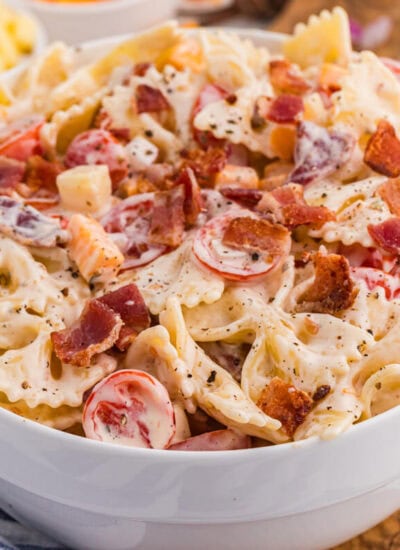 Bowl of Million Dollar Pasta Salad with bowtie pasta, crispy bacon, cheese cubes, cherry tomatoes, and red onion in creamy ranch dressing.