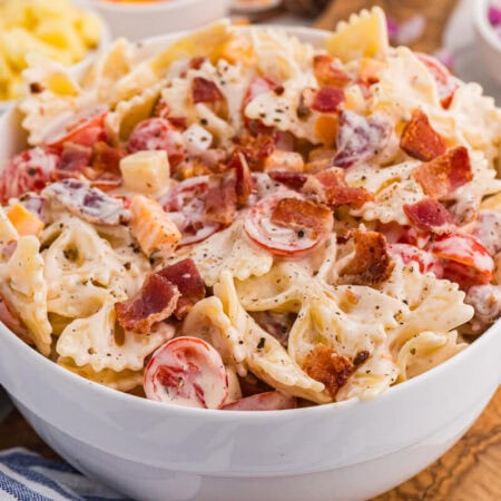 Bowl of Million Dollar Pasta Salad with bowtie pasta, crispy bacon, cheese cubes, cherry tomatoes, and red onion in creamy ranch dressing.