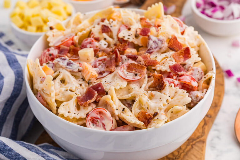 Bowl of Million Dollar Pasta Salad with bowtie pasta, crispy bacon, cheese cubes, cherry tomatoes, and red onion in creamy ranch dressing.