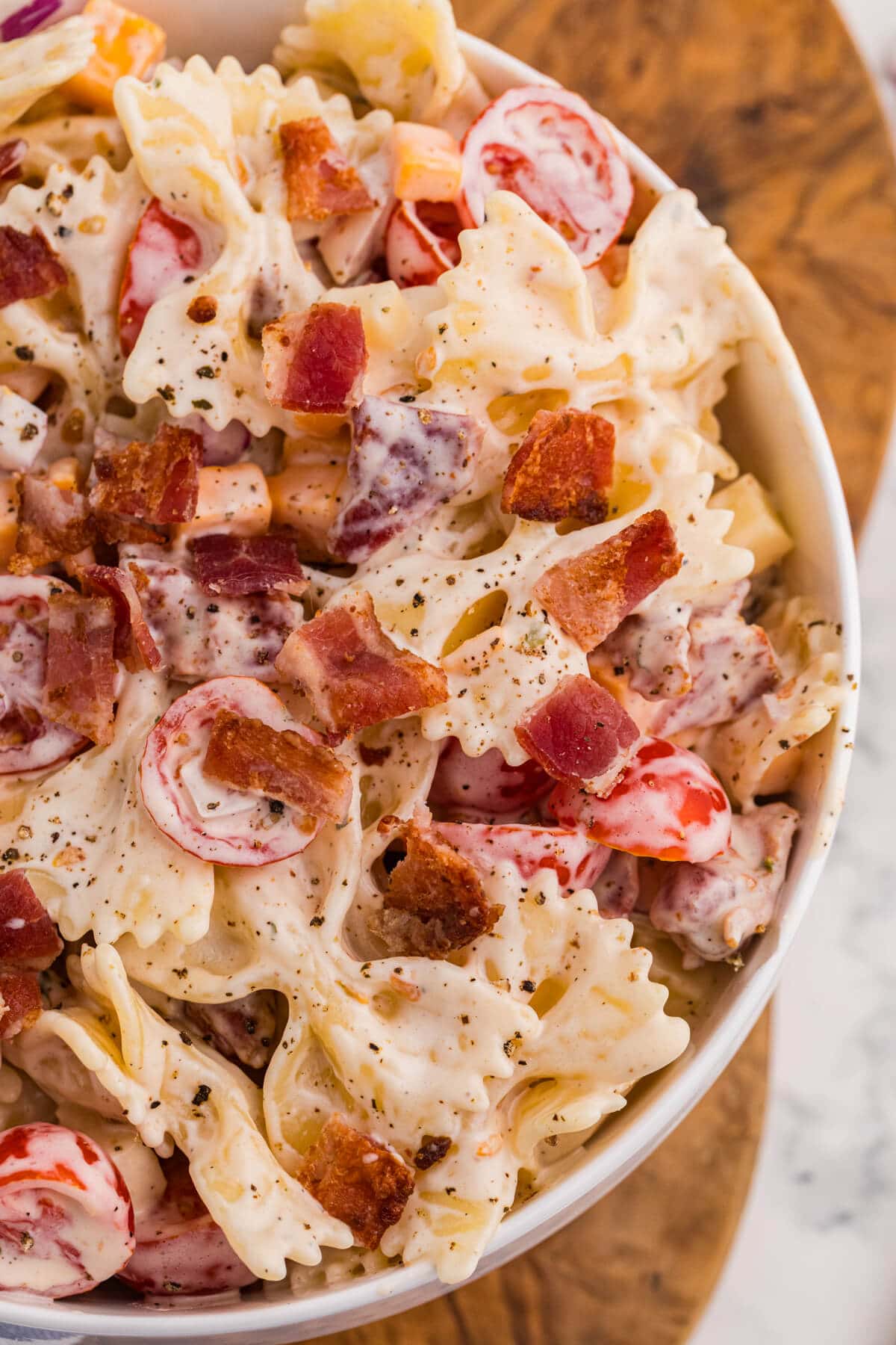 Close-up of Million Dollar Pasta Salad with creamy bowtie pasta, crispy bacon, cheese cubes, cherry tomatoes, and red onion.