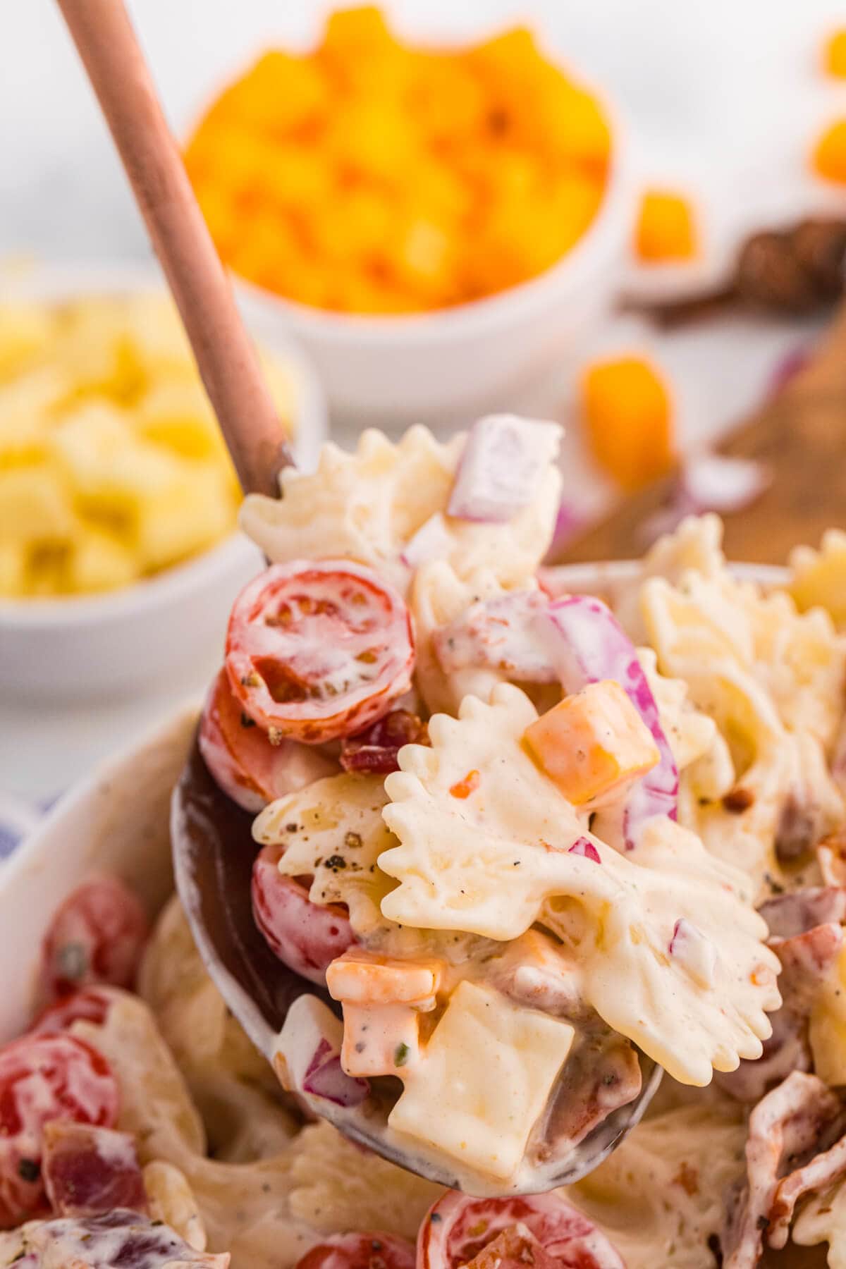 Serving spoon filled with Million Dollar Pasta Salad made with bowtie pasta, bacon, cheese cubes, cherry tomatoes, and red onion in creamy ranch dressing.