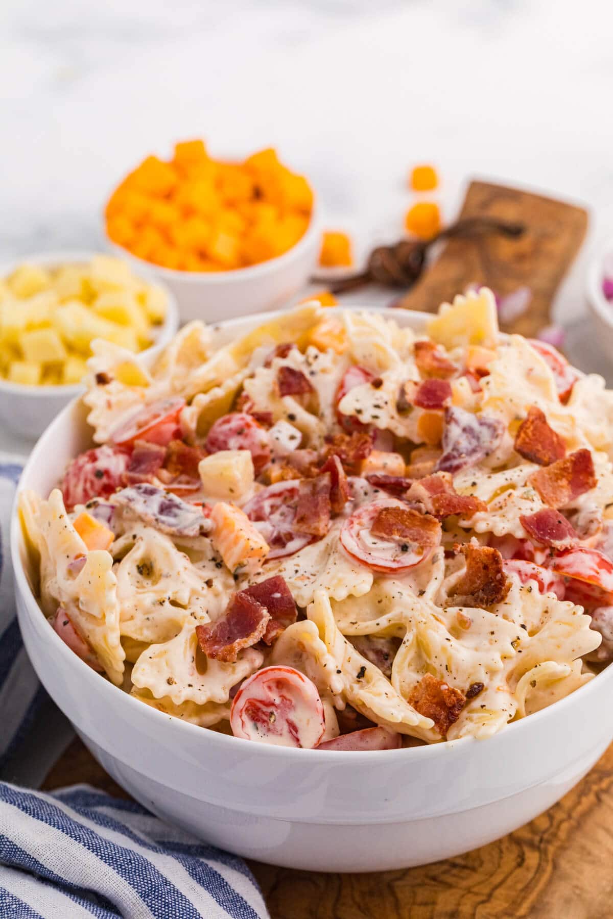 Close-up of Million Dollar Pasta Salad with bowtie pasta, crispy bacon, cheese cubes, cherry tomatoes, and red onion in a creamy ranch dressing.