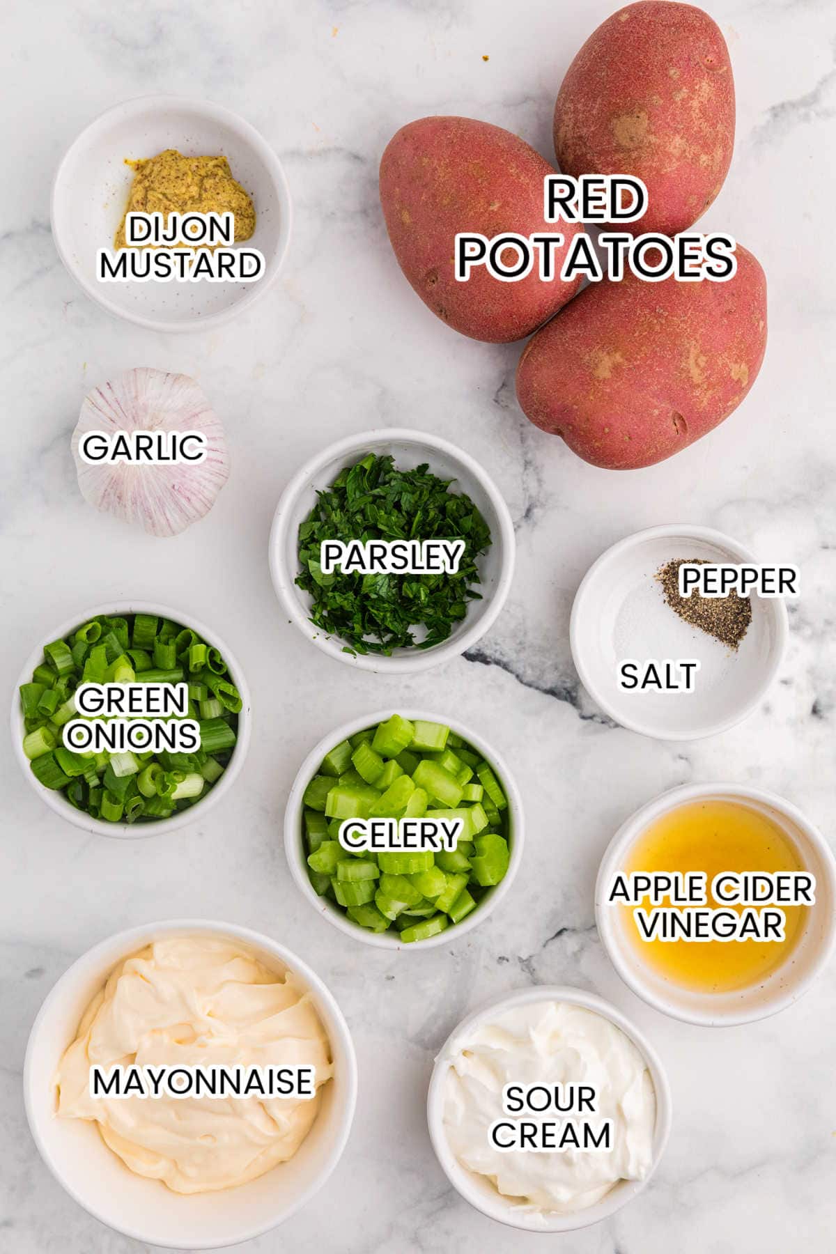 Ingredients for roasted garlic potato salad, including red potatoes, garlic, mayonnaise, sour cream, Dijon mustard, apple cider vinegar, celery, green onions, parsley, salt, and pepper.