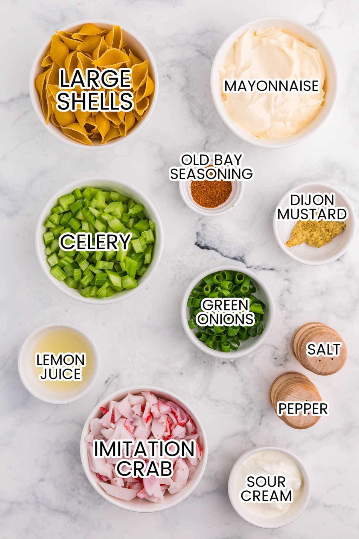 Ingredients for crab pasta salad including large shells, imitation crab, celery, green onions, mayonnaise, sour cream, lemon juice, Dijon mustard, Old Bay, salt, and pepper.