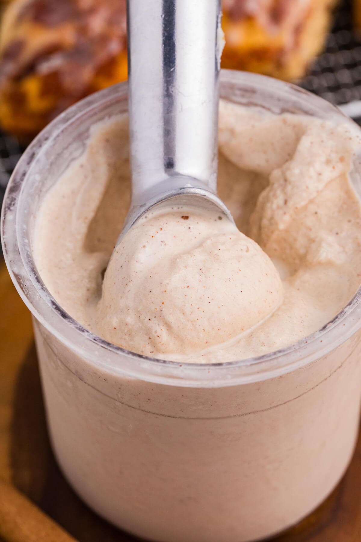 Ice cream scoop lifting creamy cinnamon roll ice cream from a Ninja CREAMi pint.