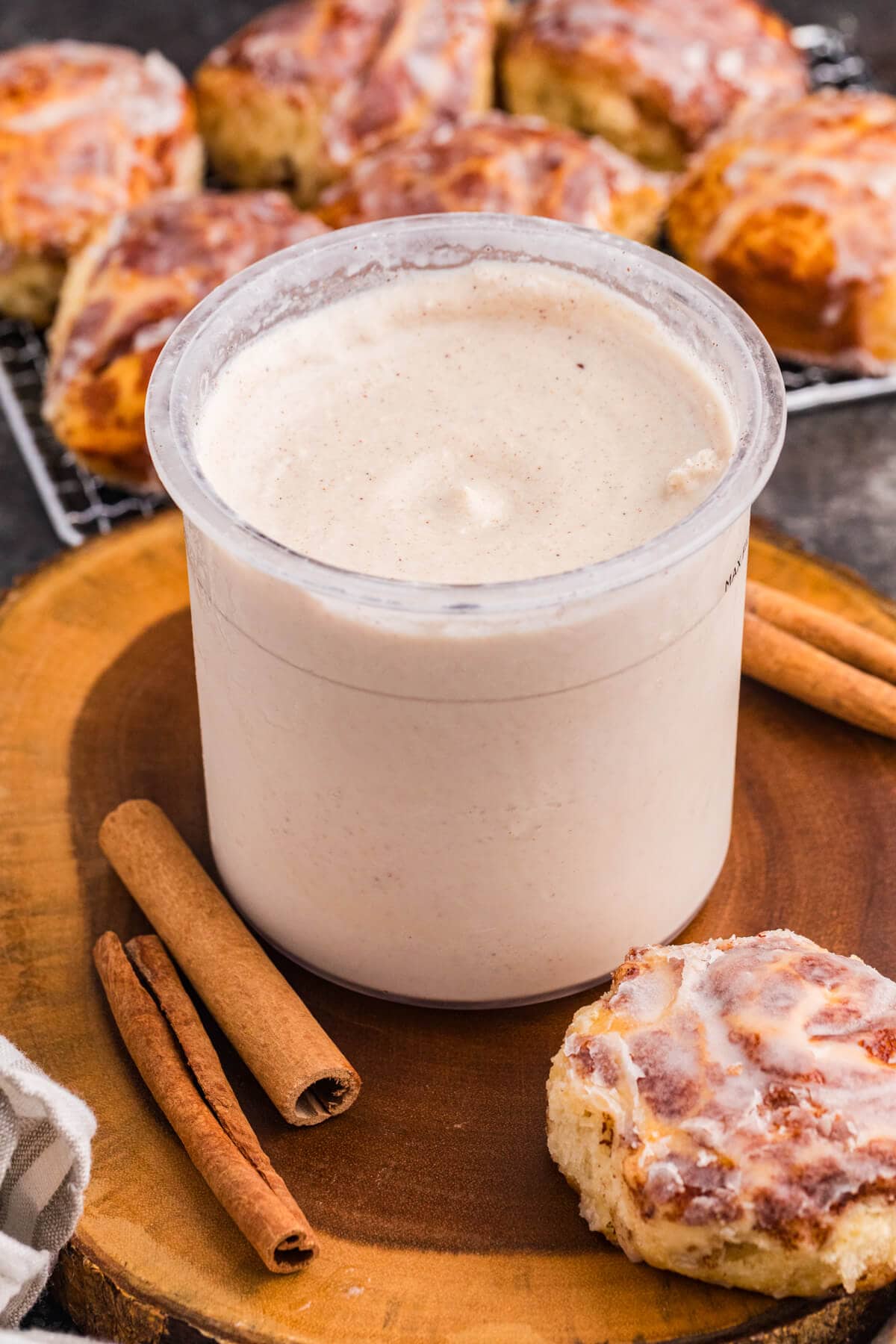 Ninja CREAMi pint filled with cinnamon roll ice cream beside cinnamon sticks and glazed cinnamon rolls.