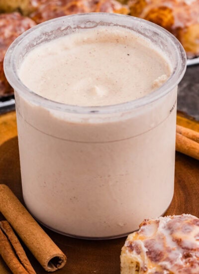 Cinnamon roll ice cream in a Ninja CREAMi pint surrounded by cinnamon sticks and glazed cinnamon rolls.