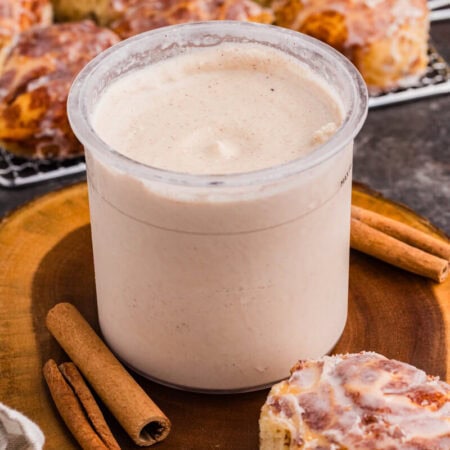 Cinnamon roll ice cream in a Ninja CREAMi pint surrounded by cinnamon sticks and glazed cinnamon rolls.
