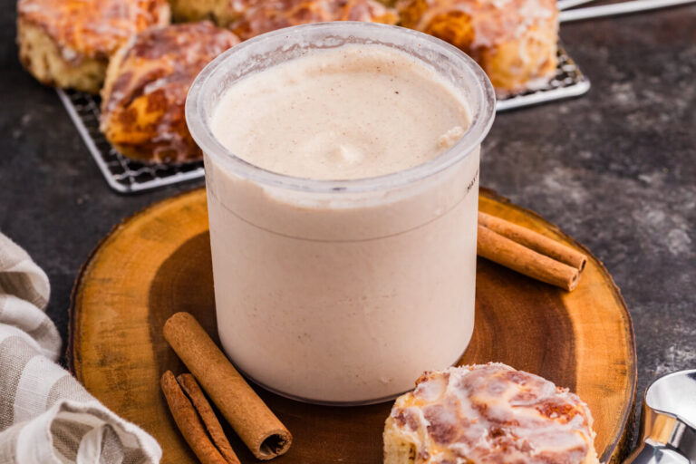Cinnamon roll ice cream in a Ninja CREAMi pint surrounded by cinnamon sticks and glazed cinnamon rolls.