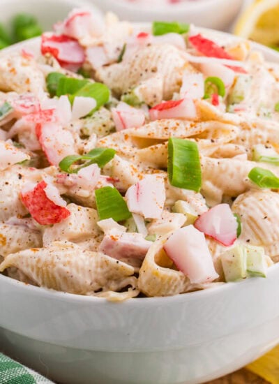 Crab pasta salad with imitation crab, shell pasta, celery, and green onions in a creamy Old Bay dressing, served with lemon wedges.