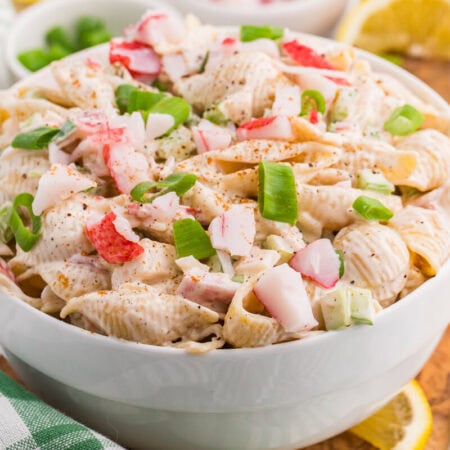 Crab pasta salad with imitation crab, shell pasta, celery, and green onions in a creamy Old Bay dressing, served with lemon wedges.