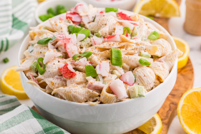Crab pasta salad with imitation crab, shell pasta, celery, and green onions in a creamy Old Bay dressing, served with lemon wedges.