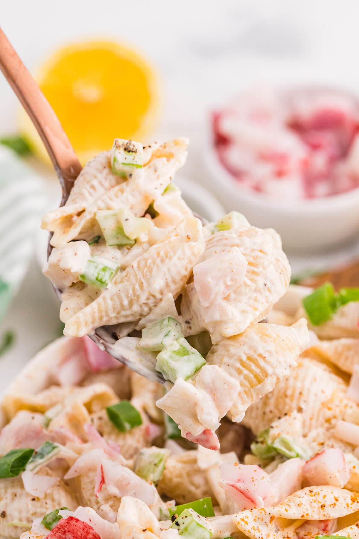 Spoonful of creamy crab pasta salad with shell pasta, imitation crab, celery, and green onions.