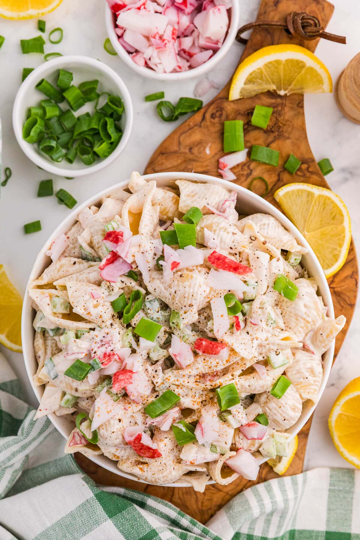 Crab pasta salad with imitation crab, shell pasta, celery, and green onions in a creamy dressing, garnished with lemon wedges.