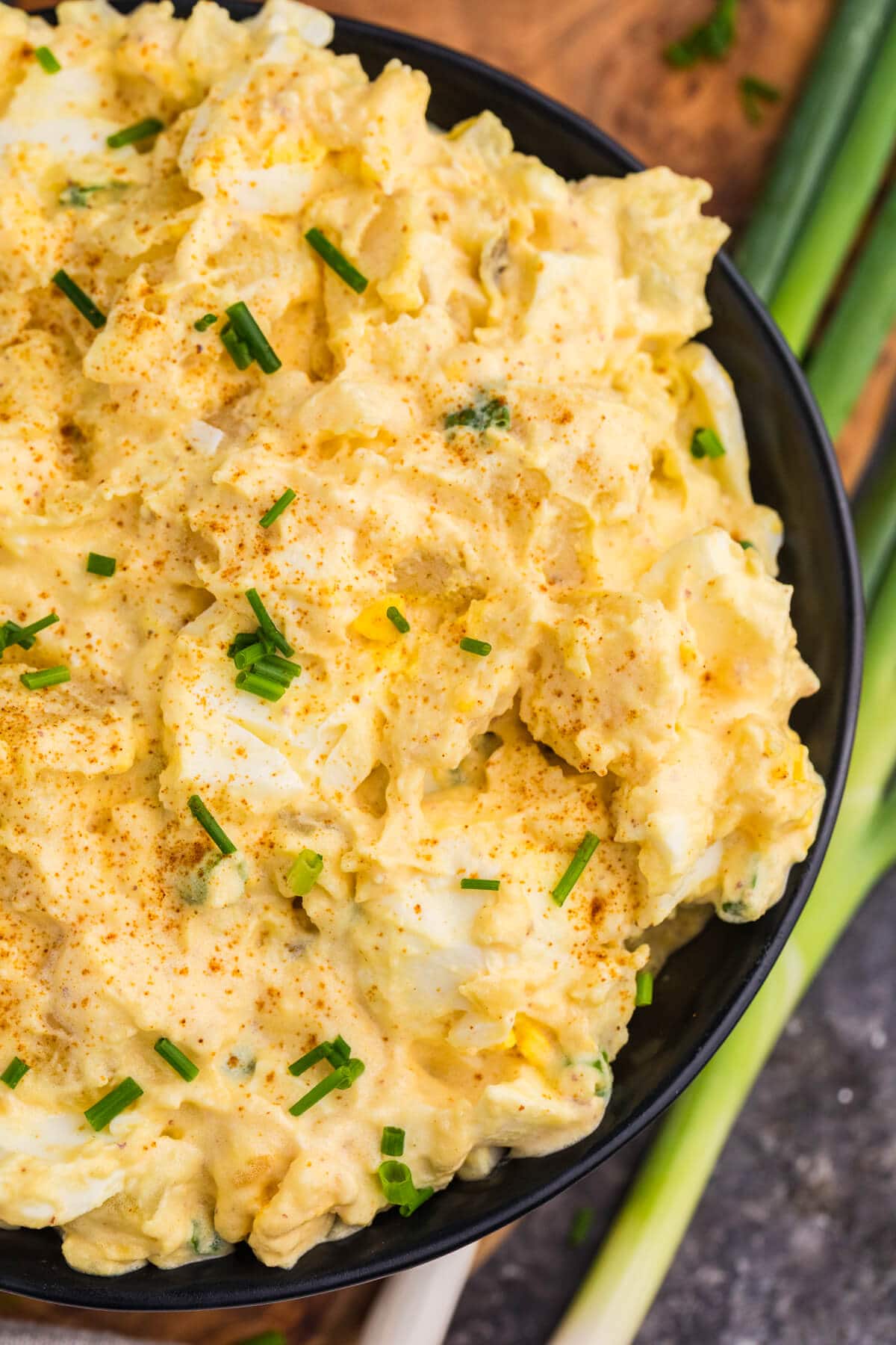 Close-up of creamy Deviled Egg Potato Salad with chunks of egg and potato, topped with paprika and chopped chives.