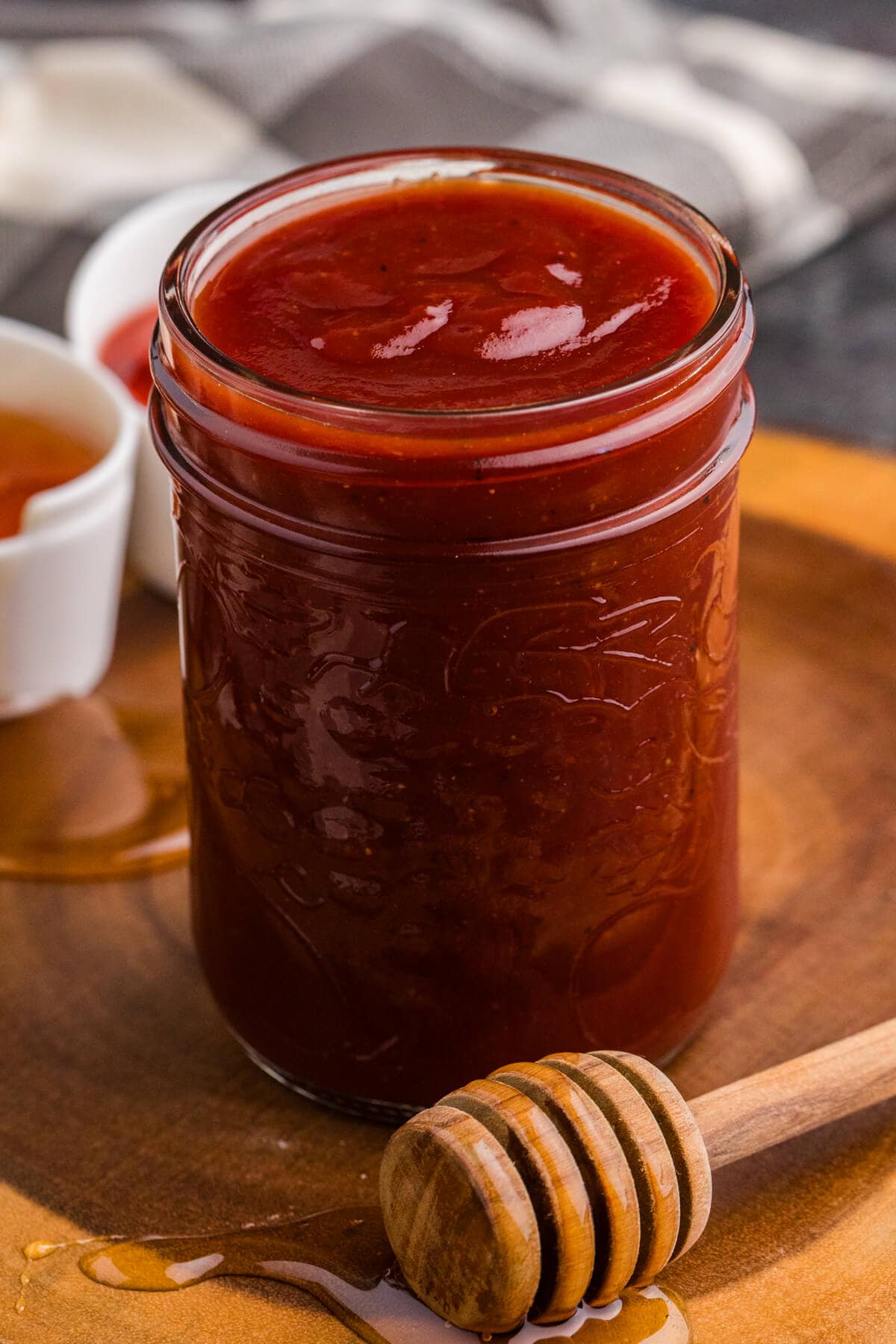 Jar of homemade Honey Sriracha BBQ Sauce with a honey dipper on a wooden board.